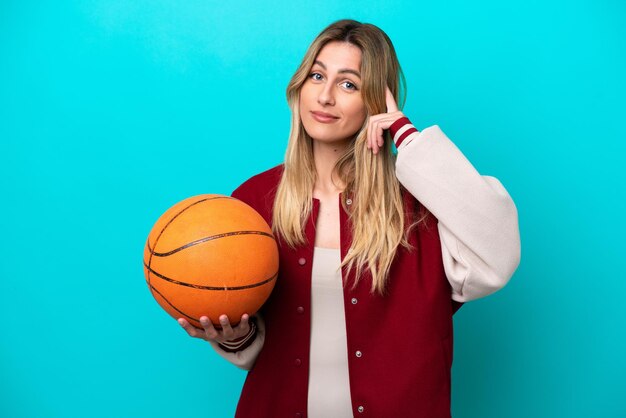 Jonge kaukasische basketbalspelervrouw die op blauwe achtergrond wordt geïsoleerd en een idee denkt