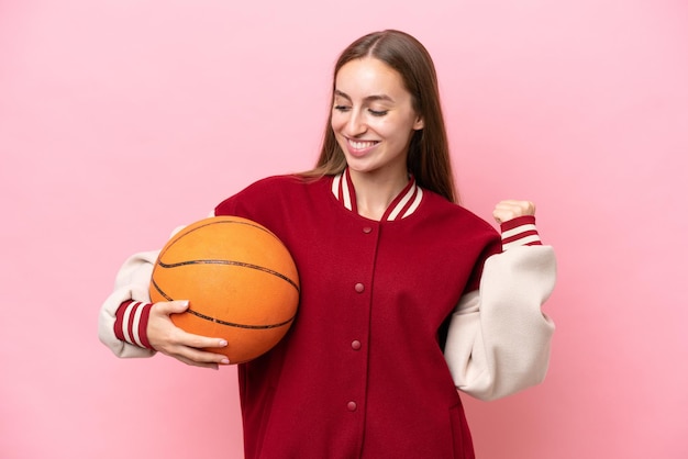 Jonge kaukasische basketbalspelervrouw over geïsoleerd op roze achtergrond die een overwinning viert