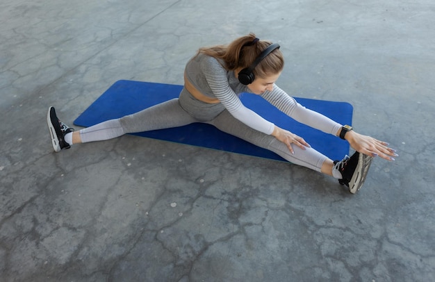 Jonge kaukasische blonde fitnessvrouw oefent zich uit terwijl ze op een mat op een betonnen vloer zit Gezonde levensstijl