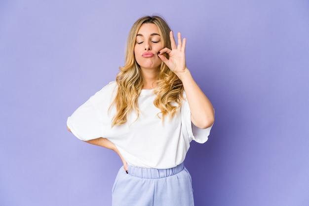 Jonge kaukasische blonde vrouw die met vingers op lippen een geheim houdt.