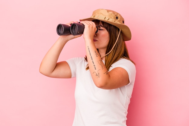 Jonge kaukasische bochtige vrouw met verrekijker geïsoleerd op roze background