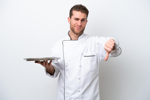 Jonge Kaukasische chef-kok met dienblad geïsoleerd op een witte achtergrond met duim omlaag met negatieve expression