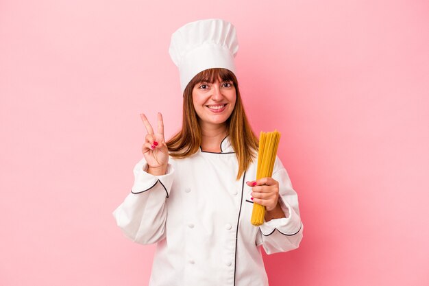 Jonge Kaukasische chef-kok vrouw met pasta geïsoleerd op roze achtergrond met nummer twee met vingers.