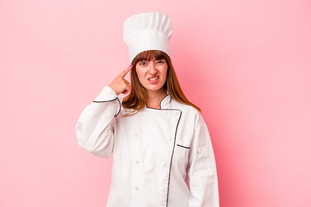 Jonge kaukasische chef-kokvrouw die op roze achtergrond wordt geïsoleerd die een teleurstellingsgebaar met wijsvinger toont.