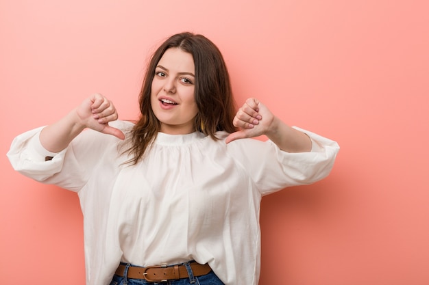 Jonge Kaukasische curvy vrouw die zich tegen roze bevindt