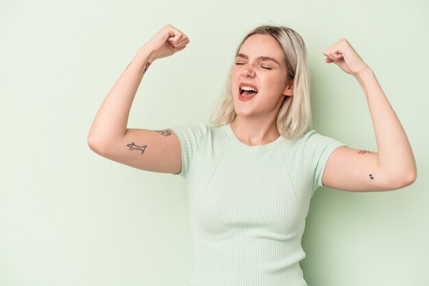 Jonge kaukasische die vrouw op groene achtergrond wordt geïsoleerd die vuist opheft na een overwinning, winnaarconcept.