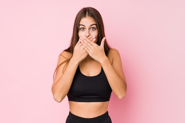 Jonge Kaukasische fitness vrouw die geïsoleerde sport doet geschokt behandelend mond met handen.