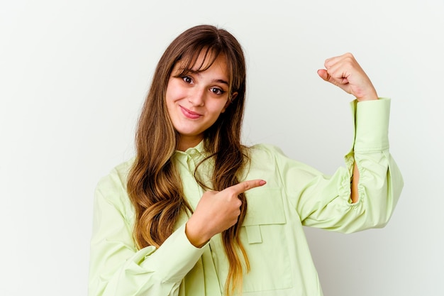 Jonge kaukasische leuke vrouw die op witte achtergrond wordt geïsoleerd die sterktegebaar met wapens toont, symbool van vrouwelijke macht