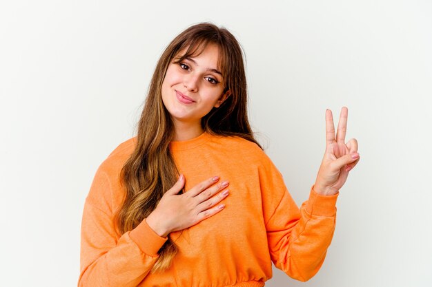 Jonge kaukasische leuke vrouw die op witte muur wordt geïsoleerd die een eed aflegt, hand op borst legt.