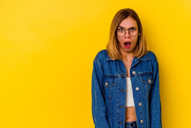 Jonge kaukasische magere vrouw die op gele muur wordt geïsoleerd die wegens iets dat zij heeft gezien wordt geschokt