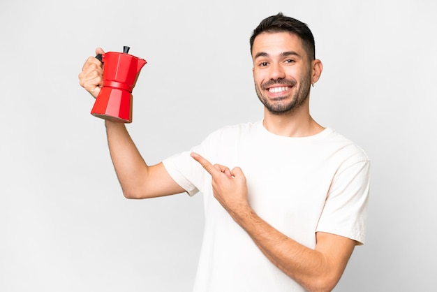 Jonge kaukasische mens die koffiepot over geïsoleerde witte achtergrond houdt en het richt