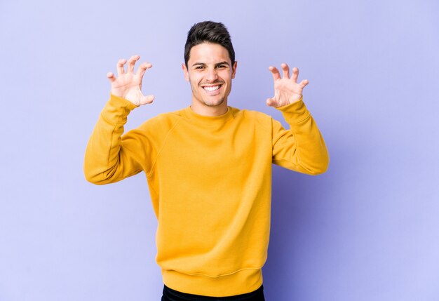 Jonge kaukasische mens die op purpere muur klauwen toont die een kat imiteren