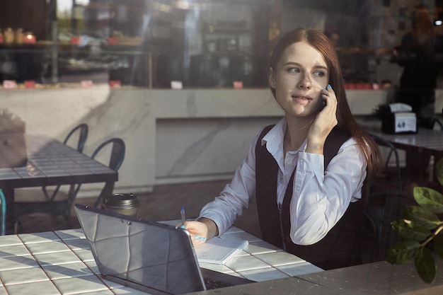 Jonge kaukasische mooie vrouw zittend aan tafel van coffeeshop bellen met smartphone
