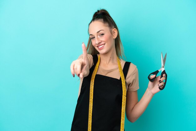 Jonge kaukasische naaistervrouw die op blauwe achtergrond wordt geïsoleerd die een vinger toont en opheft