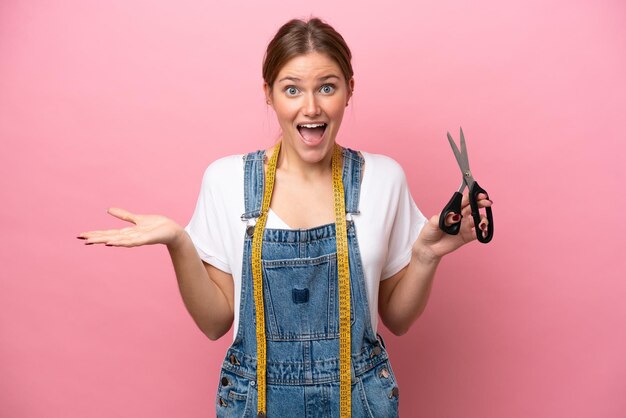 Jonge kaukasische naaistervrouw die op roze achtergrond met geschokte gezichtsuitdrukking wordt geïsoleerd