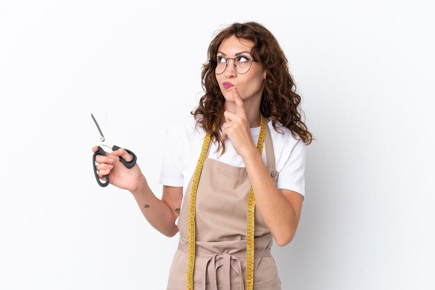 Jonge kaukasische naaistervrouw die op witte achtergrond wordt geïsoleerd die twijfels heeft terwijl het opzoeken