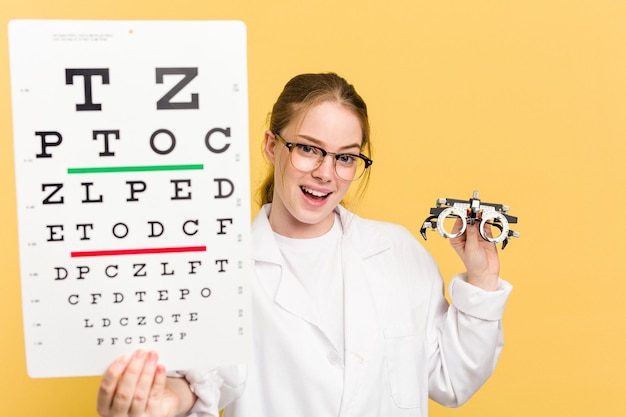 Jonge kaukasische oogartsvrouw die een oogonderzoek doet dat op gele achtergrond wordt geïsoleerd