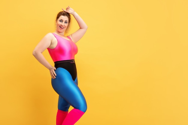 Jonge Kaukasische plus size vrouwelijke model opleiding op gele muur. Kopieerruimte. Concept van sport, gezonde levensstijl, positief lichaam, mode, stijl. Stijlvolle vrouw die zelfverzekerd en cool poseert.