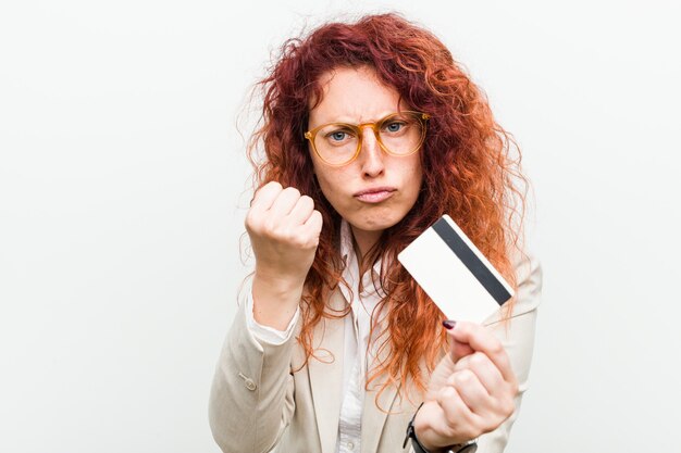 Foto jonge kaukasische roodharigevrouw die een creditcard houden die vuist tonen aan camera