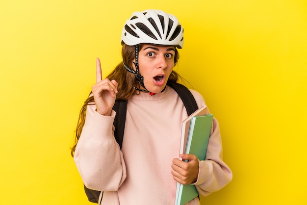 Jonge kaukasische studentenvrouw die een fietshelm draagt die op gele achtergrond wordt geïsoleerdd die een idee, inspiratieconcept heeft.