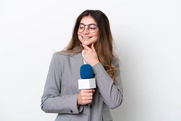 Jonge Kaukasische tv-presentator vrouw geïsoleerd op een witte achtergrond op zoek naar de kant en lachend