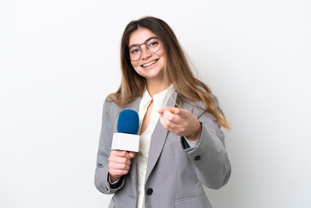 Jonge kaukasische tv-presentatorvrouw geïsoleerd op een witte achtergrond die naar voren wijst met gelukkige uitdrukking