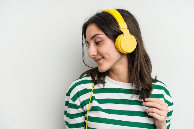 Jonge kaukasische vrouw die aan muziek luistert die op witte achtergrond wordt geïsoleerd