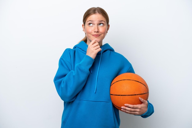 Jonge kaukasische vrouw die basketbal speelt die op witte achtergrond wordt geïsoleerd en omhoog kijkt