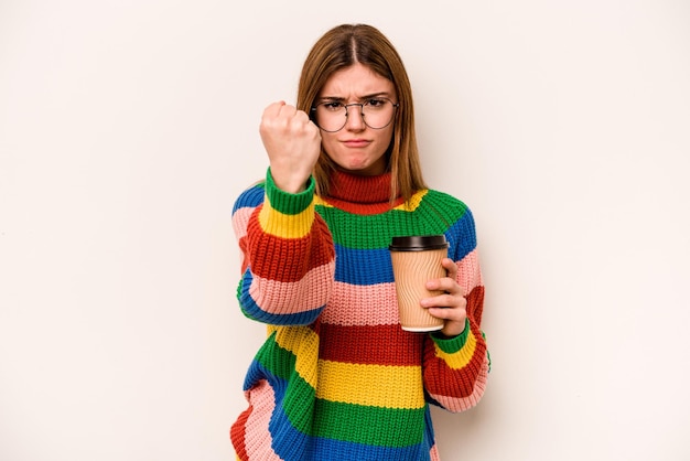 Jonge kaukasische vrouw die een afhaalkoffie houdt die op witte achtergrond wordt geïsoleerd die vuist toont aan camera agressieve gezichtsuitdrukking