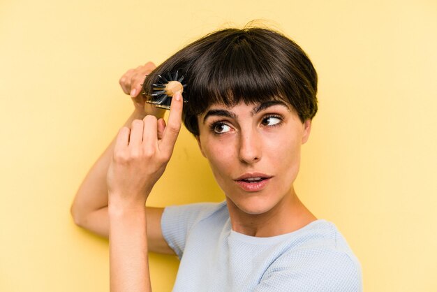 Jonge kaukasische vrouw die een borstelhaar houdt dat op gele achtergrond wordt geïsoleerd