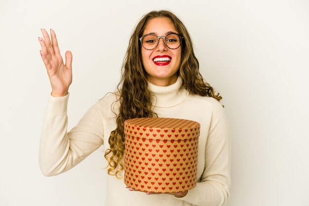 Jonge kaukasische vrouw die een geïsoleerde de dagdoos van hartvalentijnskaarten houdt die een aangename verrassing ontvangen, opgewekt en handen opheft.