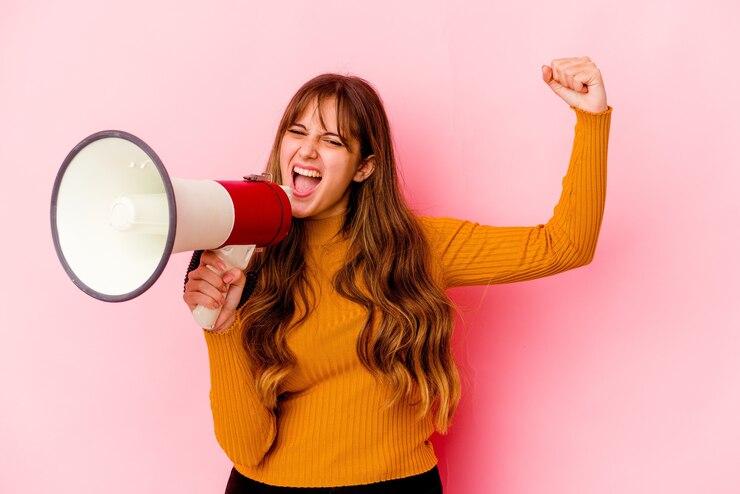 Foto jonge kaukasische vrouw die een geïsoleerde megafoon houdt die vuist opheft na een overwinning, winnaarconcept.