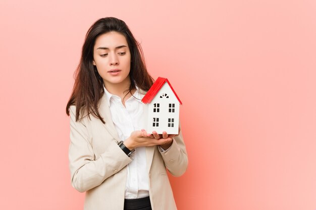 Jonge Kaukasische vrouw die een huispictogram houdt