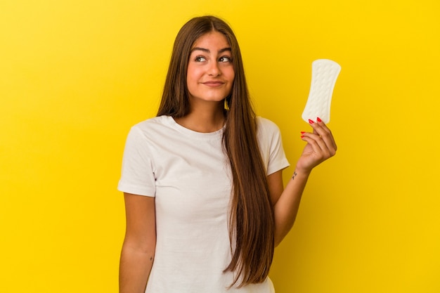 Jonge kaukasische vrouw die een kompres houdt dat op gele achtergrond wordt geïsoleerd en droomt van het bereiken van doelen en doeleinden