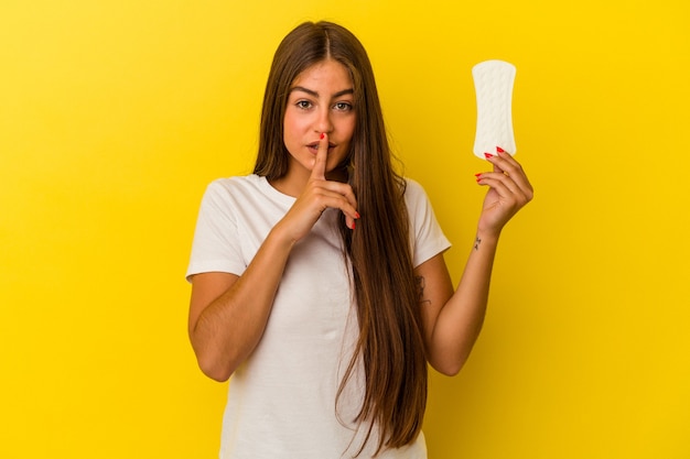 Jonge kaukasische vrouw die een kompres houdt dat op gele achtergrond wordt geïsoleerd en een geheim houdt of om stilte vraagt.