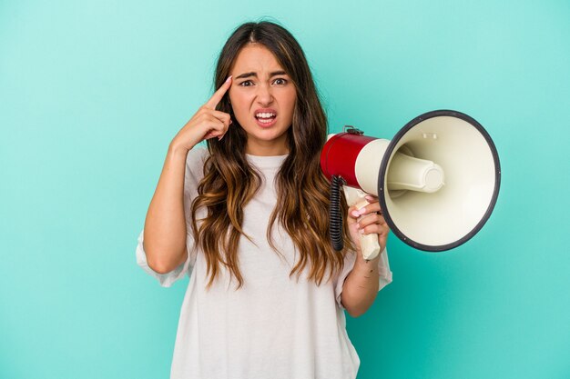 Jonge kaukasische vrouw die een megafoon houdt die op blauwe achtergrond wordt geïsoleerd die een teleurstellingsgebaar met wijsvinger toont.