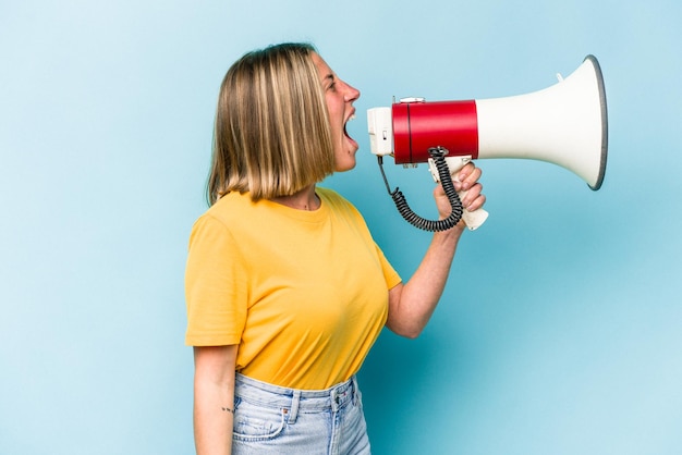 Jonge kaukasische vrouw die een megafoon houdt die op blauwe achtergrond wordt geïsoleerd