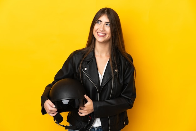 Jonge kaukasische vrouw die een motorhelm houdt die op gele achtergrond wordt geïsoleerd die een idee denkt tijdens het opzoeken