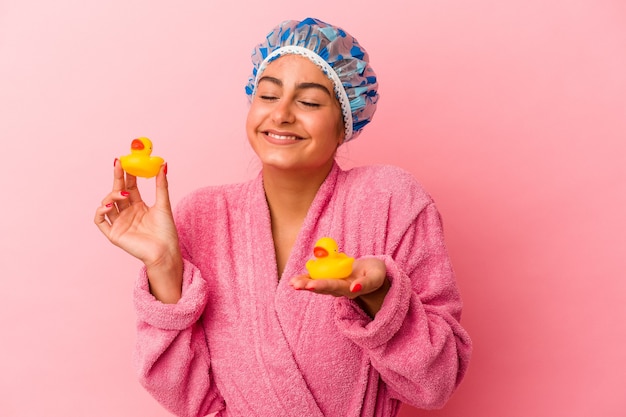 Jonge kaukasische vrouw die een plastic eend houdt die op roze achtergrond wordt geïsoleerd