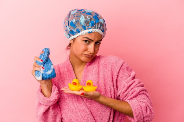 Jonge kaukasische vrouw die een plastic eend houdt die op roze achtergrond wordt geïsoleerd