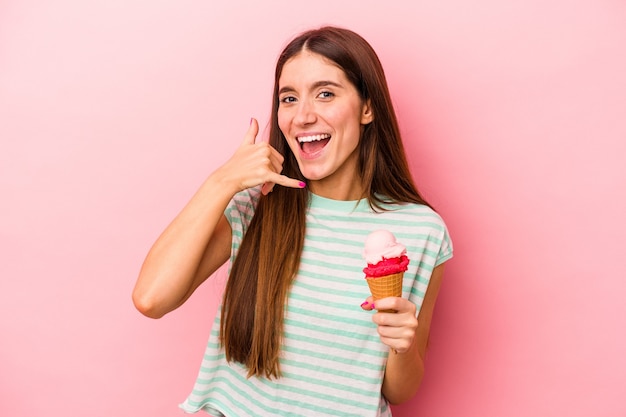 Jonge kaukasische vrouw die een roomijs houdt dat op roze achtergrond wordt geïsoleerd die een mobiel telefoongesprekgebaar met vingers toont.