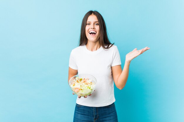 Jonge kaukasische vrouw die een salade houdt die een overwinning of een succes viert