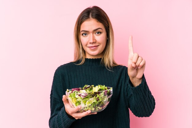 Jonge kaukasische vrouw die een salade houdt die nummer één met vinger toont.