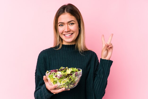 Jonge kaukasische vrouw die een salade houdt die nummer twee met vingers toont.