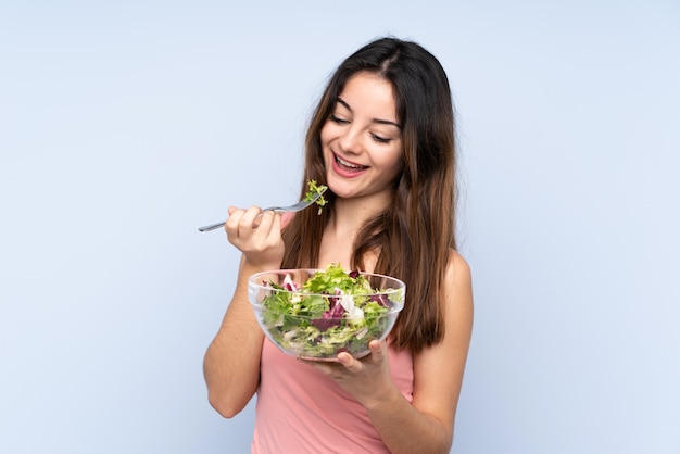 Jonge Kaukasische vrouw die een salade op blauwe muur houdt