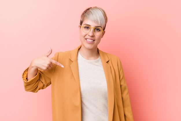 Jonge kaukasische vrouw die een toevallige bedrijfsklerenpersoon draagt die met de hand naar een overhemds exemplaarruimte richt, trots en zelfverzekerd