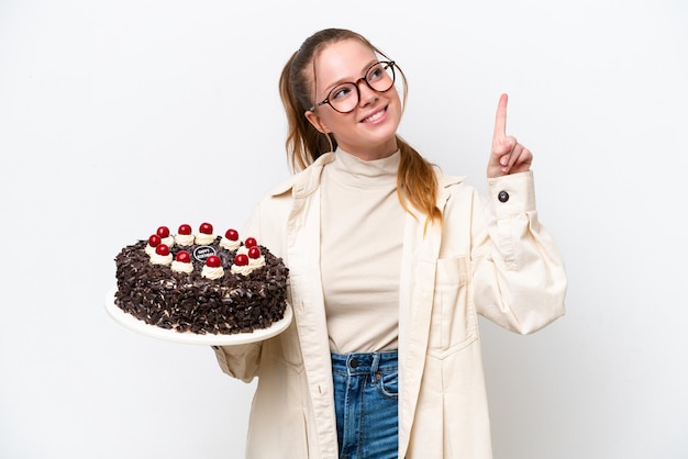 Jonge kaukasische vrouw die een verjaardagstaart houdt die op witte achtergrond wordt geïsoleerd die een groot idee benadrukt