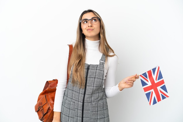 Jonge kaukasische vrouw die een vlag van het Verenigd Koninkrijk houdt die op witte achtergrond wordt geïsoleerd en omhoog kijkt