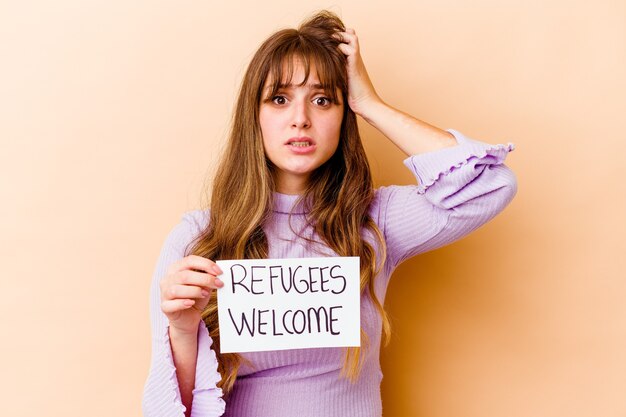 Jonge kaukasische vrouw die een vluchtelingen-welkomstbordje vasthoudt, geïsoleerd geschokt, herinnert zich een belangrijke ontmoeting.