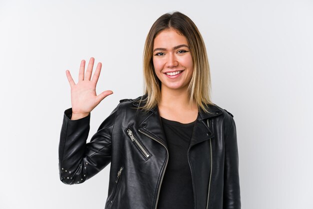 Jonge Kaukasische vrouw die een zwart leerjasje draagt dat vrolijk tonend nummer vijf met vingers glimlacht.